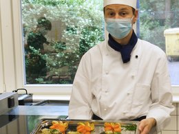 Junger Koch mit Tablet, auf dem Fisch und Gemüse angerichtet sind.