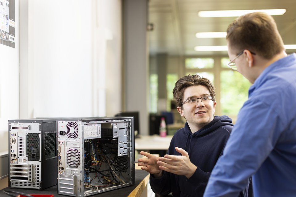 Zwei Auszubildende vor einem aufgeschraubten Computer