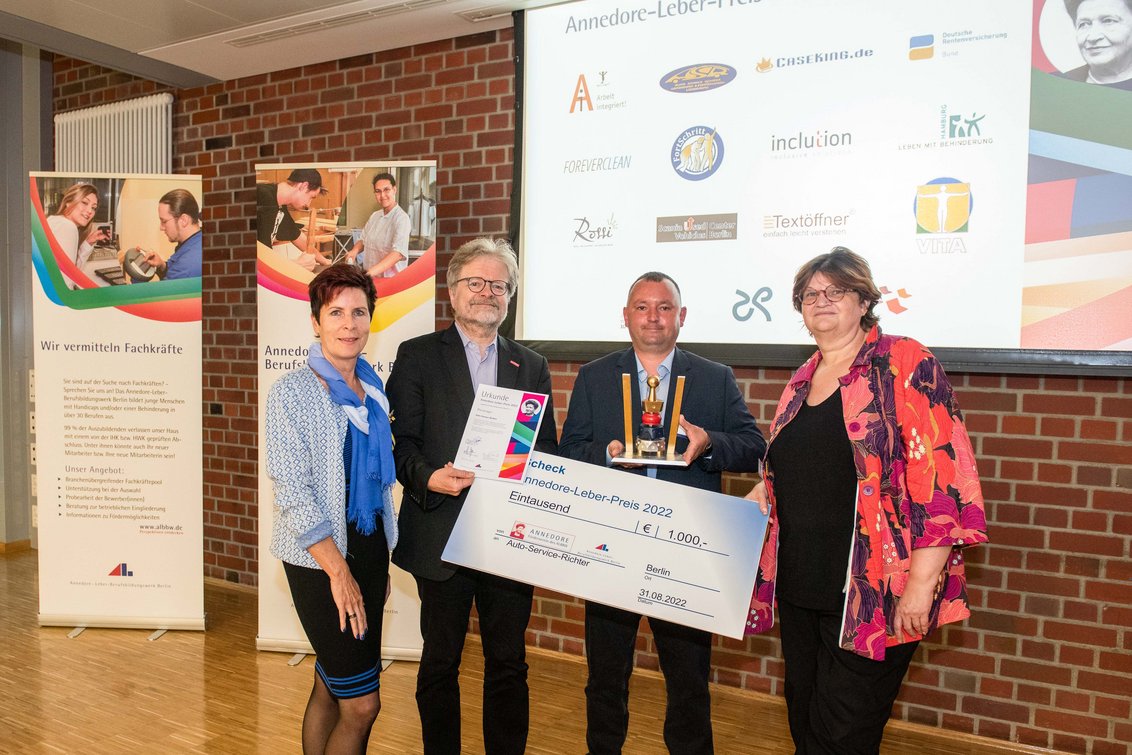 Vier Menschen mit Preisscheck, Pokal und Urkunde