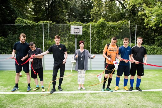 Junge Menschen stehen auf dem Fußballfeld. Eine Frau hat ein Band zur Einweihung des Feldes durchtrennt.