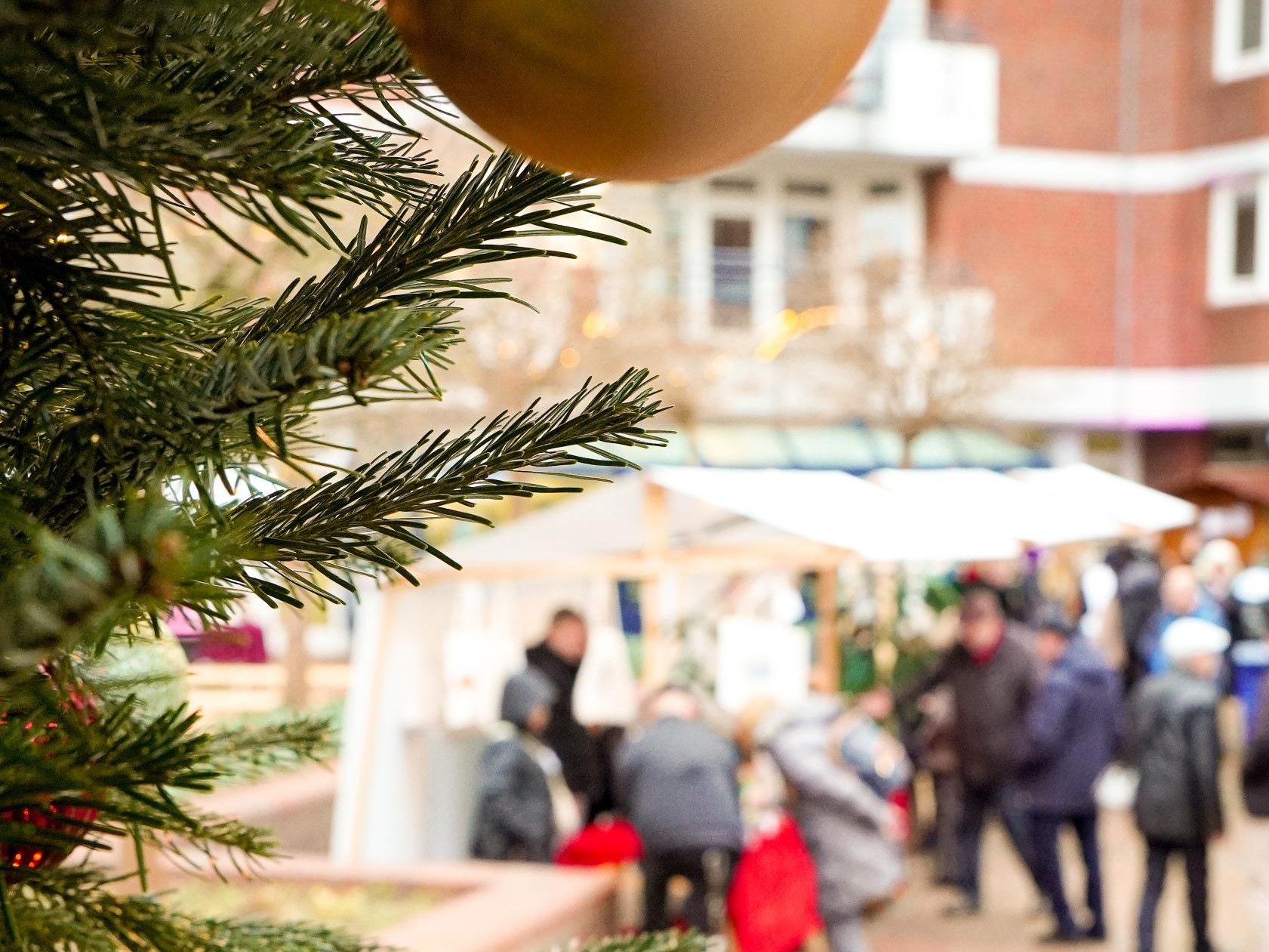 Nahaufnahme einer Weihnachtskugel am Baum, im Hintergrund Marktstände