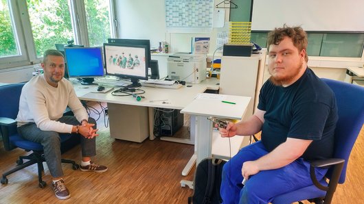Zwei Männer im Gespräch an einem PC-Arbeitsplatz.