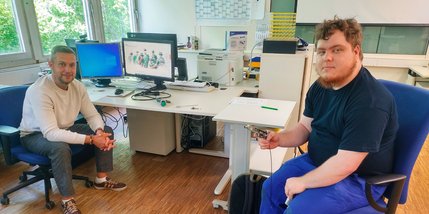Zwei Männer im Gespräch an einem PC-Arbeitsplatz.