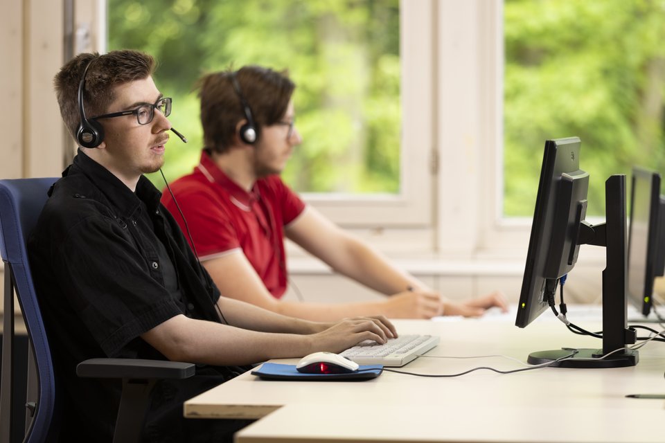 Zwei Auszubildende mit Headsets arbeiten am Computer