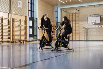 Zwei Auszubildende auf Spinning Rädern in der Turnhalle