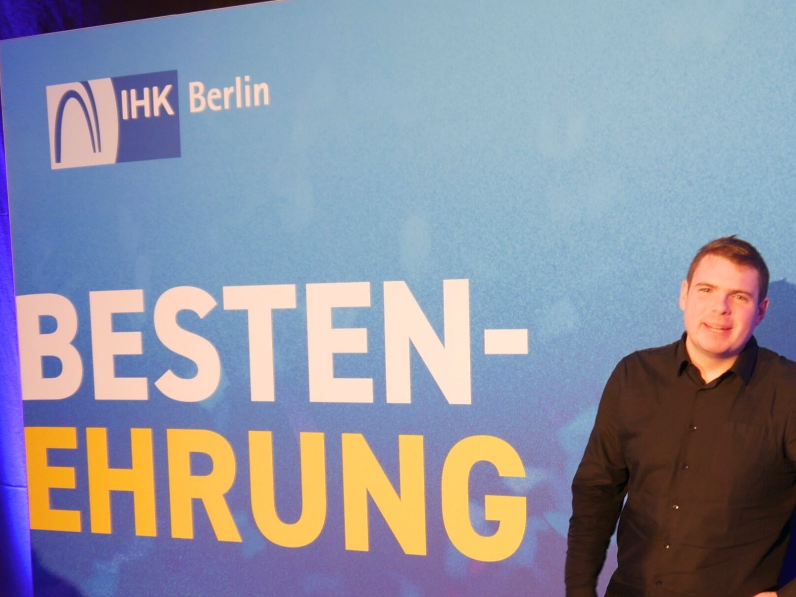 Cedric Voos posiert vor dem Plakat Bestenehrung der IHK Berlin