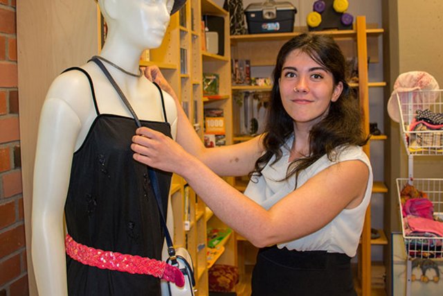 Junge Frau kleidet eine Schaufensterpuppe ein und sieht in die Kamera