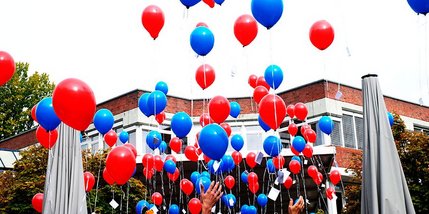 Luftballons steigen vor einem Gebäude in den Himmel