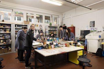 Mitarbeiter*in mit Auszubildenden beim Arbeiten mit Farben an einem großen Tisch