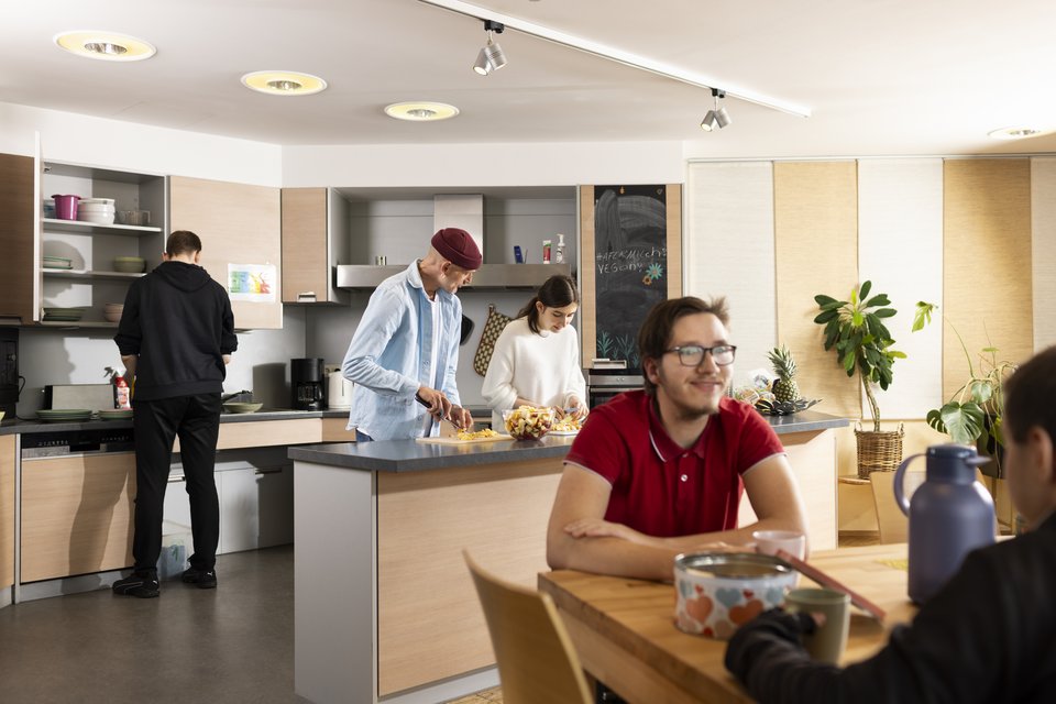 Vorbereitungen in der Küche und Unterhaltungen am Tisch im Gemeinschaftsraum