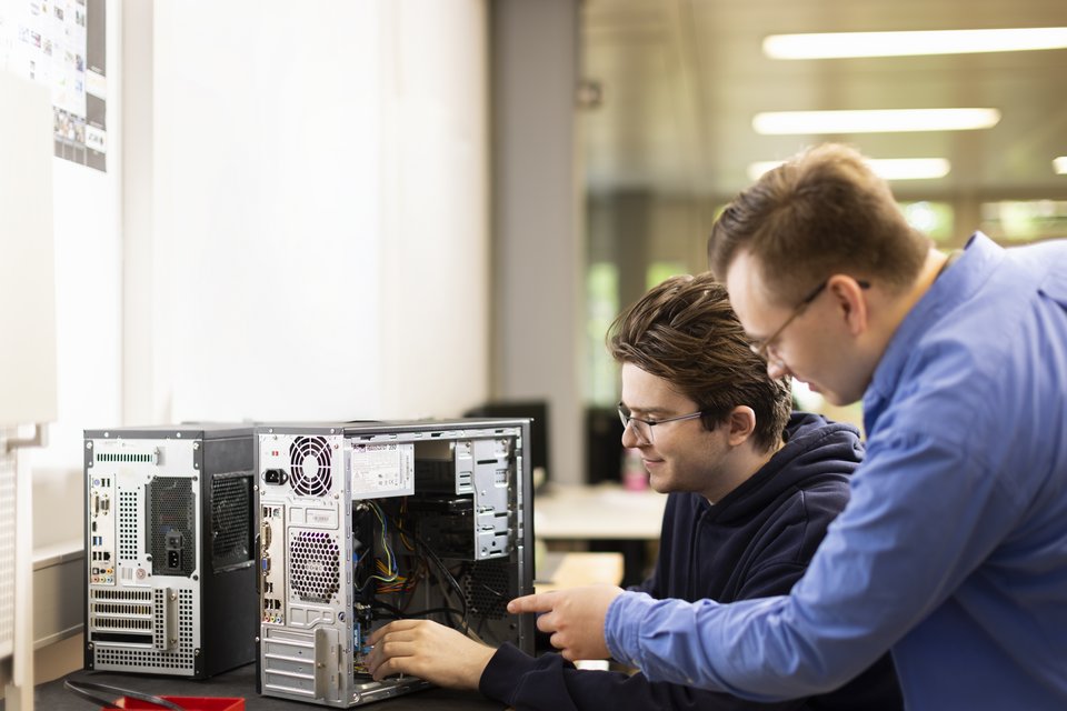 Zwei Auszubildende betrachten einen aufgeschraubten Computer.