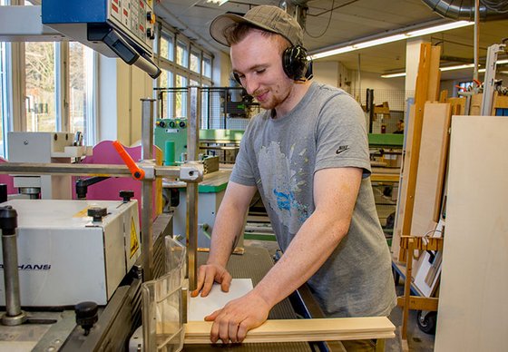 Ein junger Mann arbeitet in einer Holzwerkstatt bzw. Tischlerei.