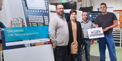Vier Menschen stehen vor einer CNC-Maschine.