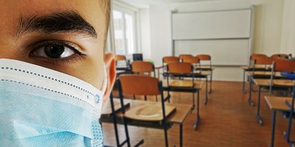 Junger Mann mit OP-Maske in einem leeren Klassenraum