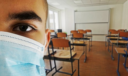 Junger Mann mit OP-Maske in einem leeren Klassenraum