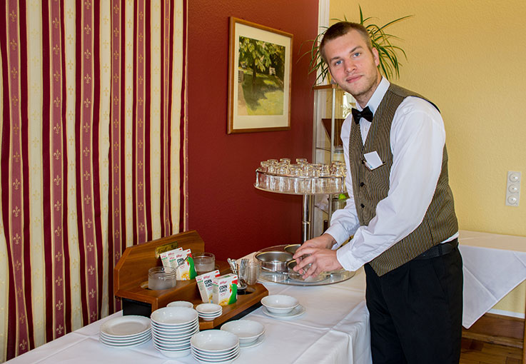 Junger Mann deckt einen Buffettisch mit Speisen und Geschirr.