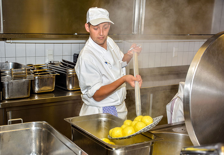 Ein Koch hält eine große Keller mit Kartoffelklößen in der Hand.