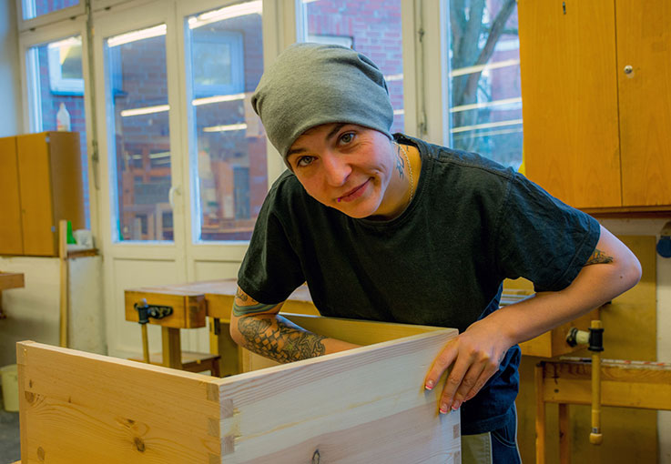 Eine Frau arbeitet an einem Werkstück aus Holz. 