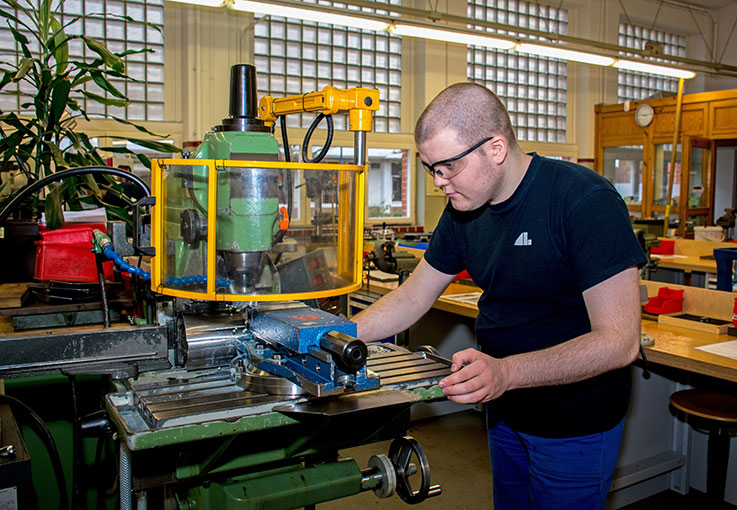 Ein junger Mann arbeitet in einer Werkhalle an einer Maschine.