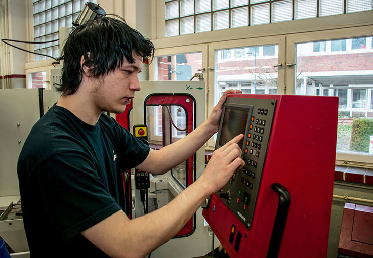 Ein Mann bedient in einer Werkhalle eine Maschine.