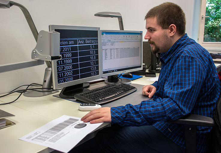 Ein Auszubildender sitzt an zwei Bildschirmen und hat Kalkulationsdateien geöffnet..