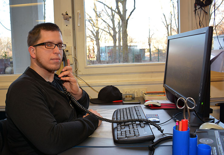 Ein Auszubildender sitzt am Computer und telefoniert mit einem Festnetztelefon.
