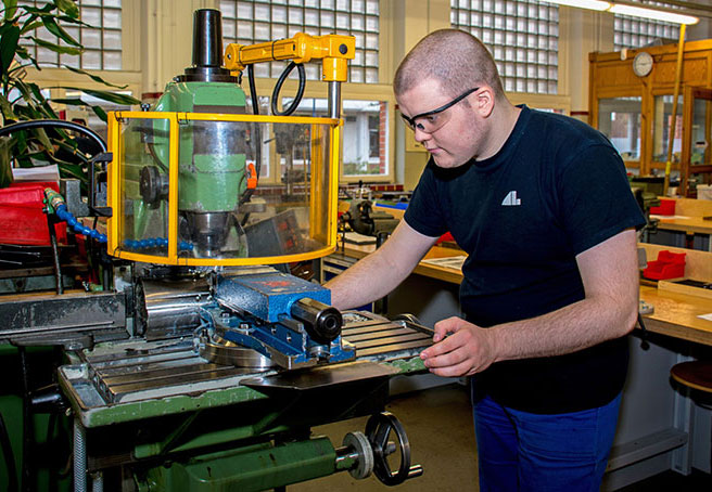 Ein Auszubildender mit Schutzausrüstung arbeitet an industrieller Maschine.