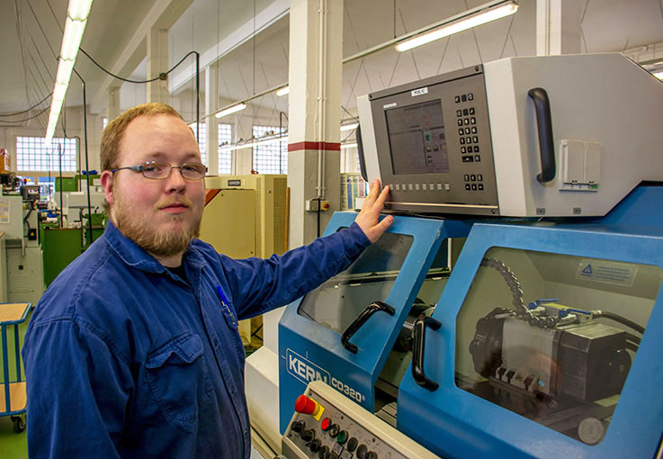 Ein Auszubildender in blauer Arbeitskleidung bedient Maschine.