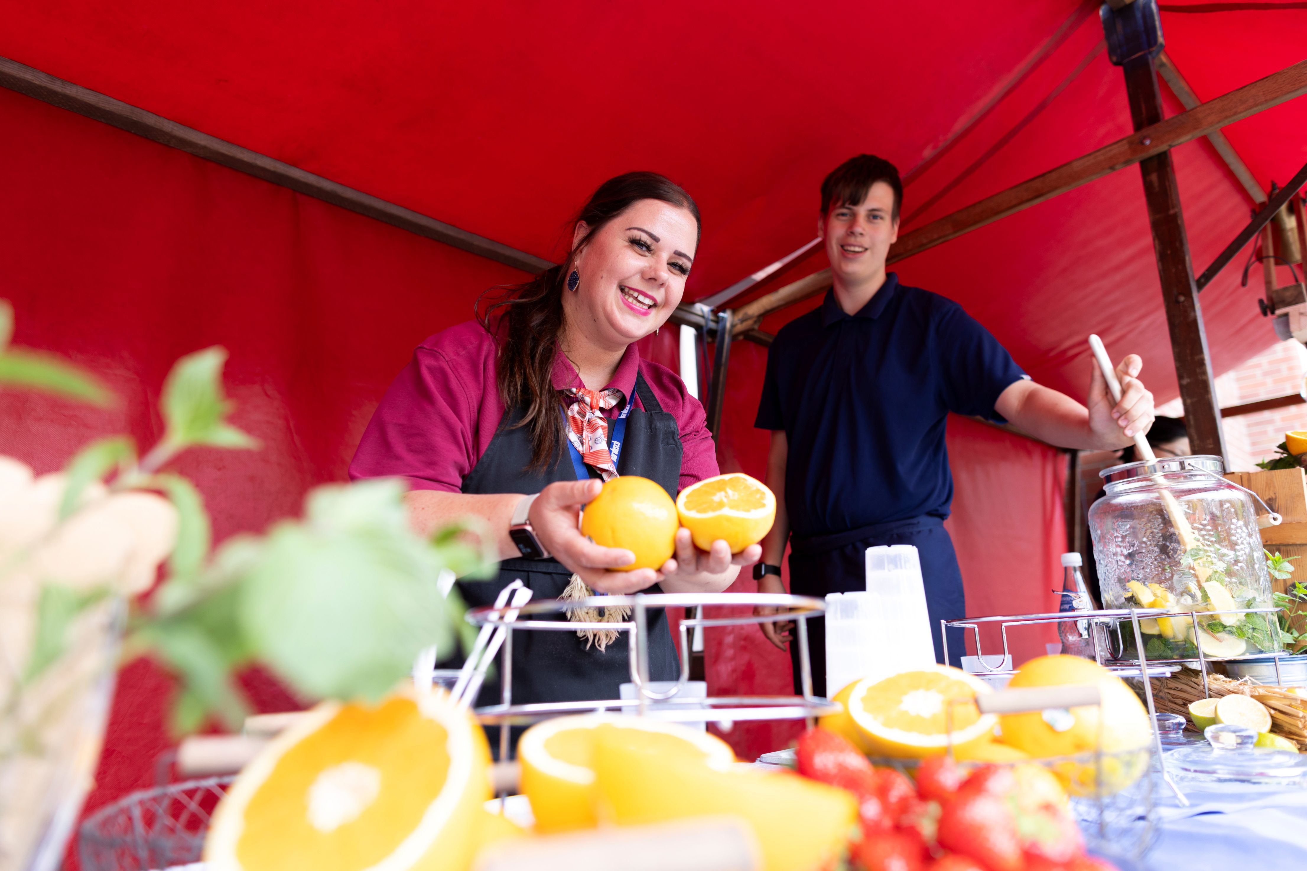Eine junge Frau hält zwei Orangen, ein junger Mann bereitet Limonade zu