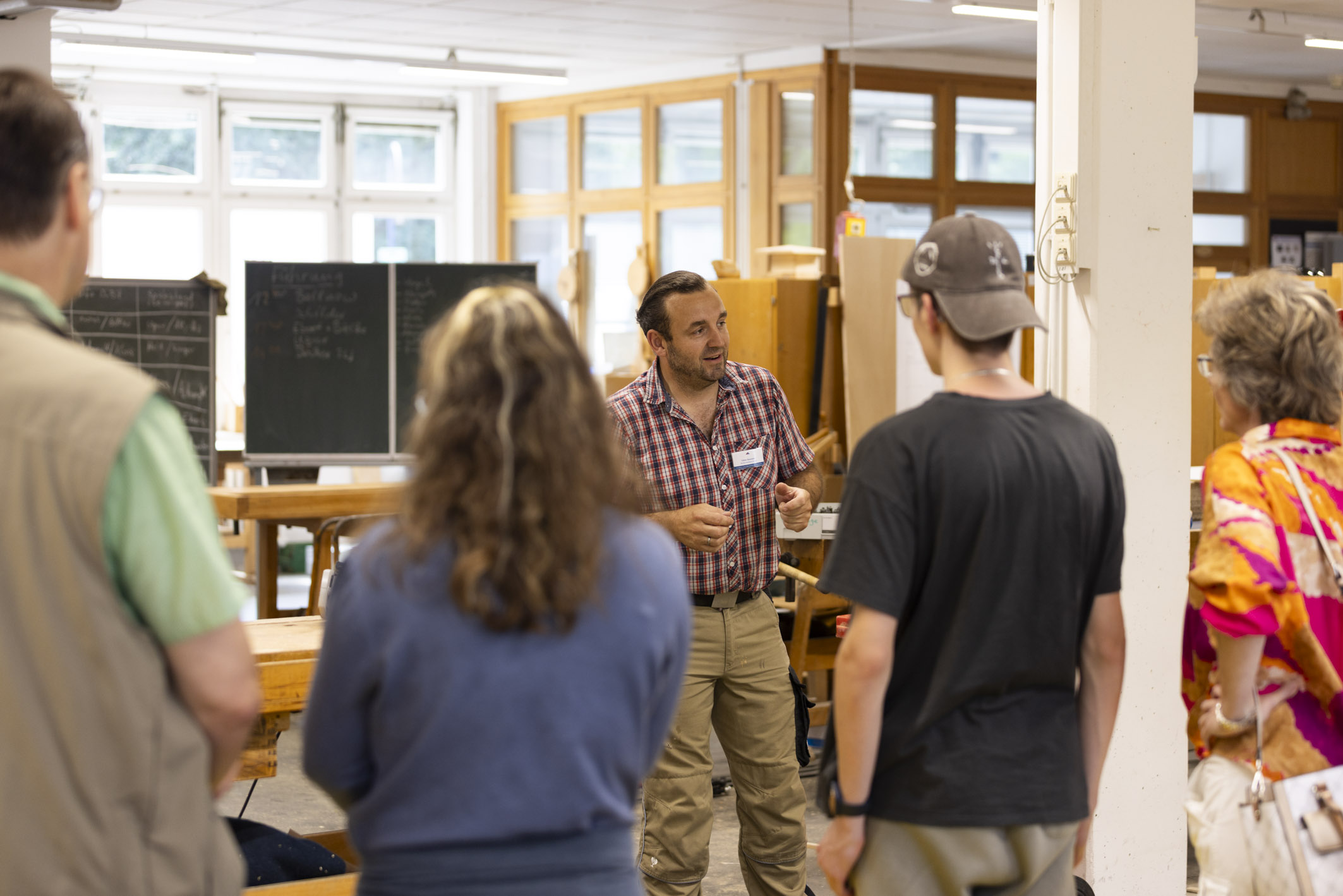 Ein Ausbilder erklärt vier Personen etwas in der Holzwerkstatt